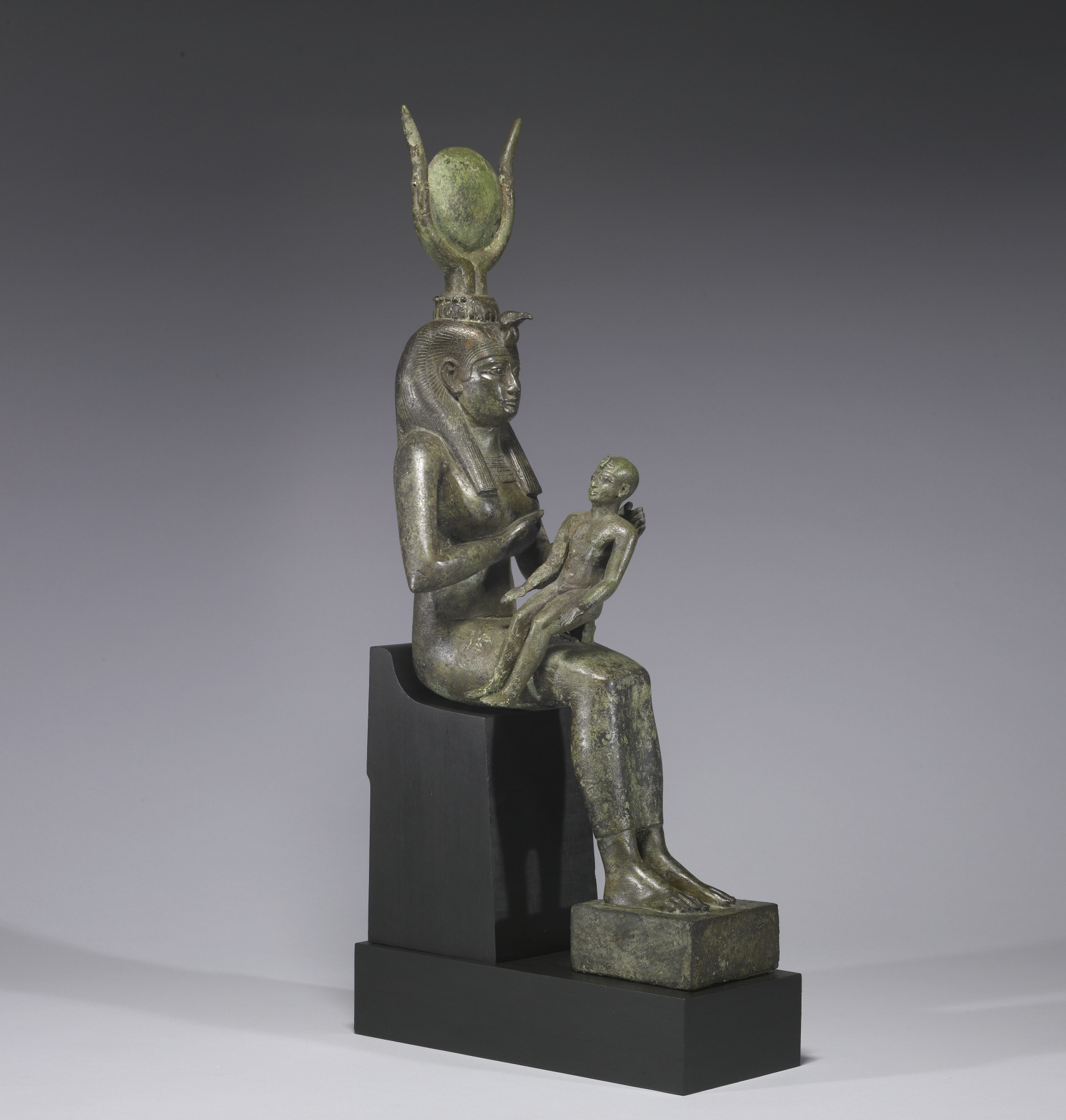 A statue made of bronze of Isis sitting and holding her son Horus.